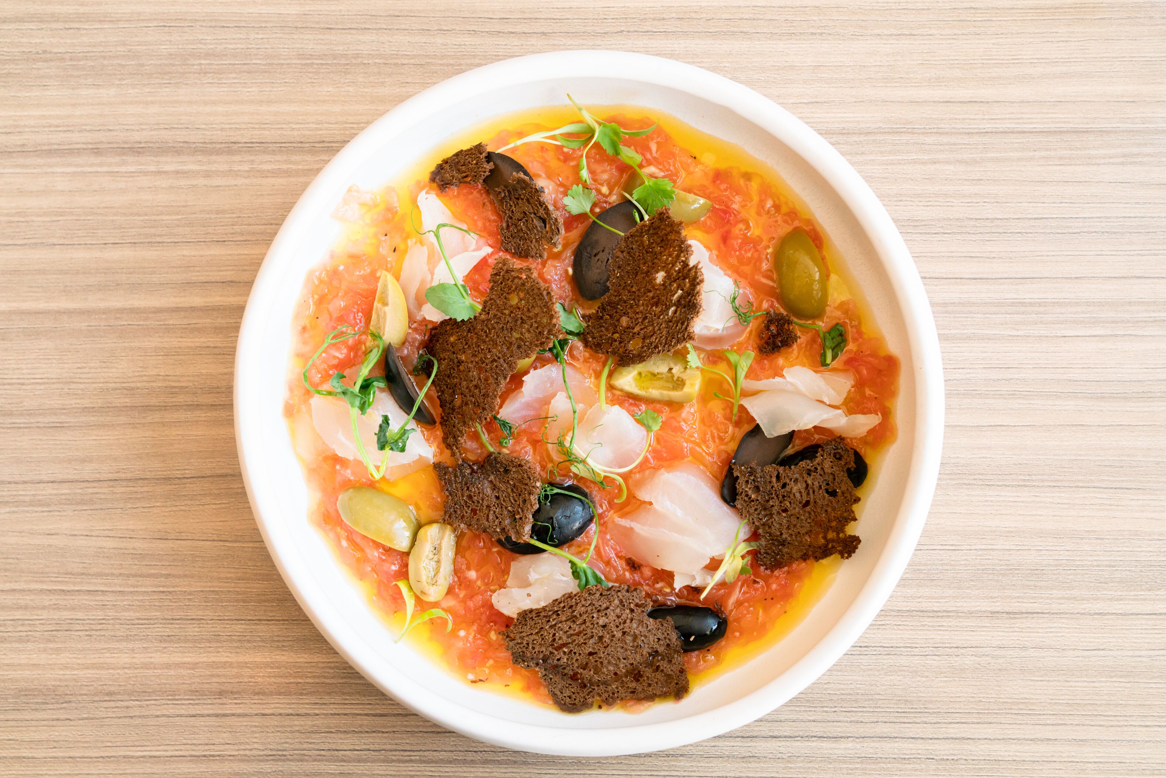 A bowl of food with various toppings on a wooden table.