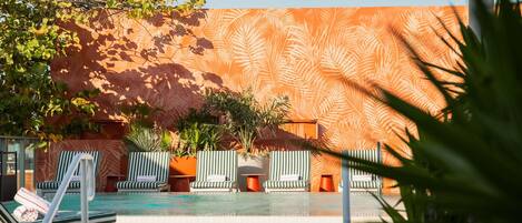 A pool area with lounge chairs, potted plants, and a patterned wall.