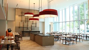 Un comedor moderno con varias mesas y sillas, una isla central y ventanas amplias que ofrecen luz natural.