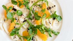 Un plat de pasta amb trossos de taronja i fulles verdes.