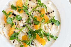 Un plato de pasta con segmentos de naranja y hojas verdes.
