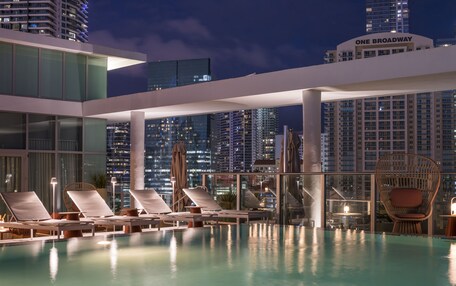 A rooftop pool area with lounge chairs and a view of One Broadway building.