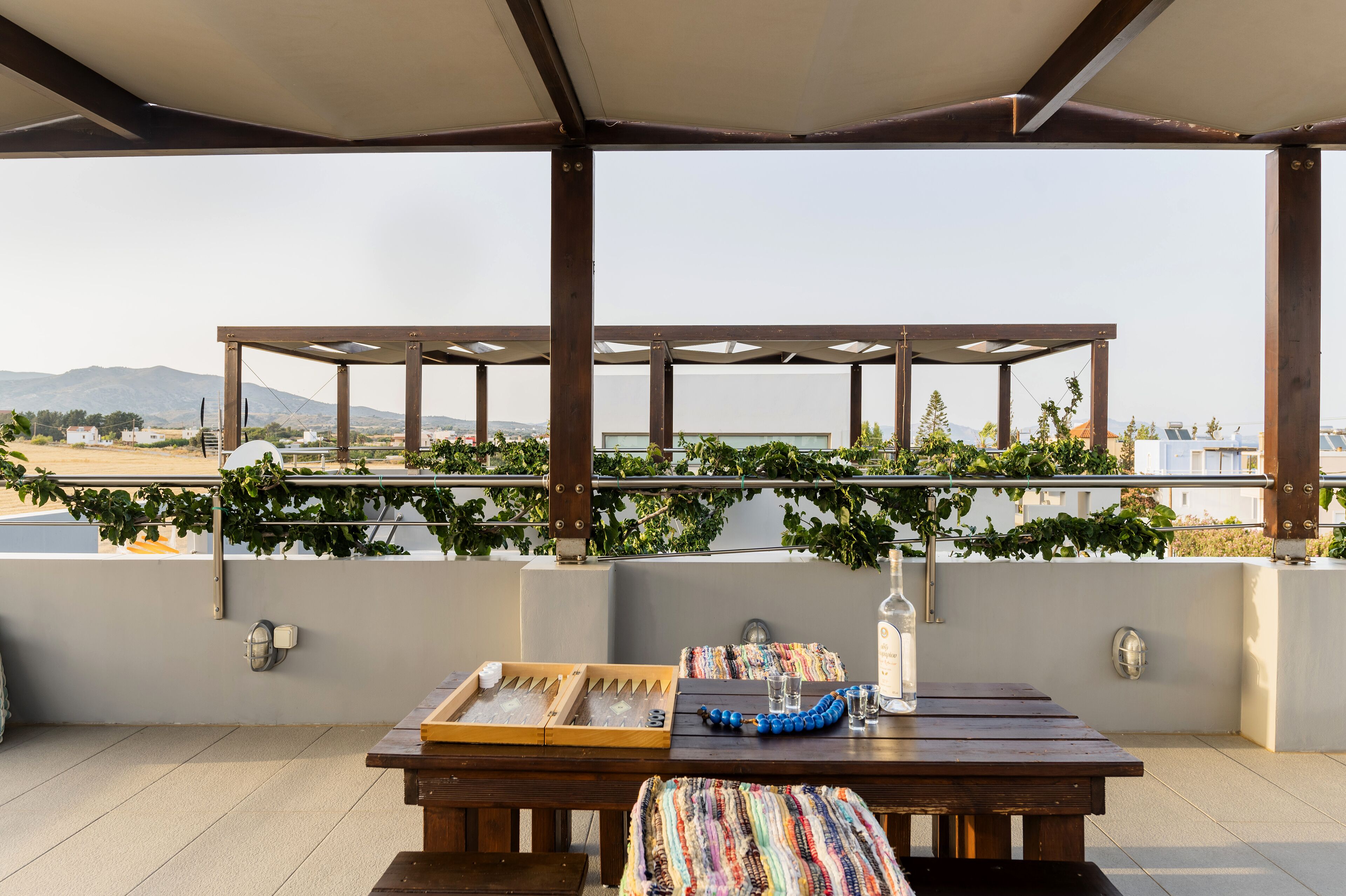 Un espacio de estar al aire libre techado con vista al paisaje, una mesa de madera con una bandeja y un vaso, y una botella.