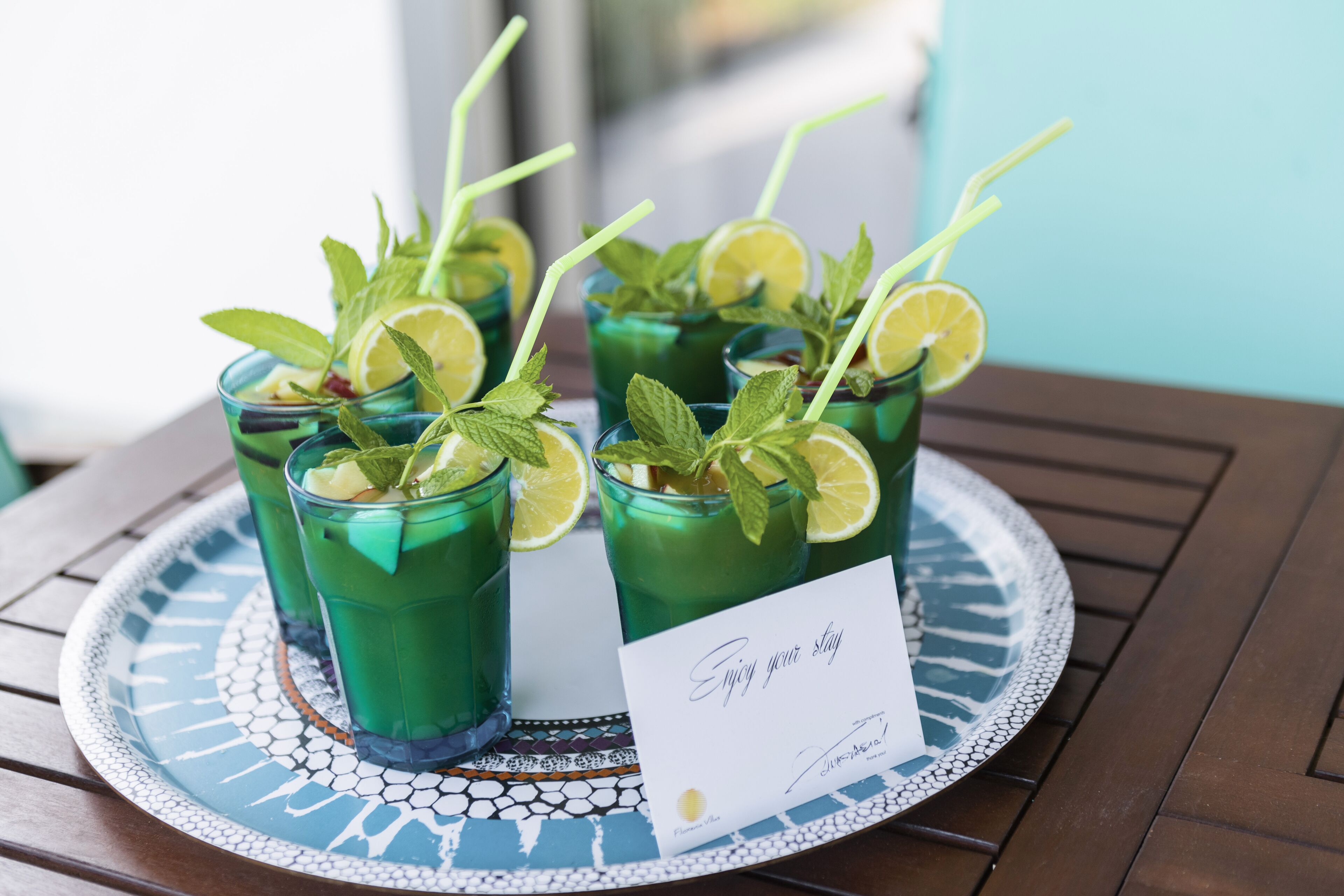 Four glasses of green beverage with lime slices and mint leaves, placed on a decorative tray with a handwritten note.