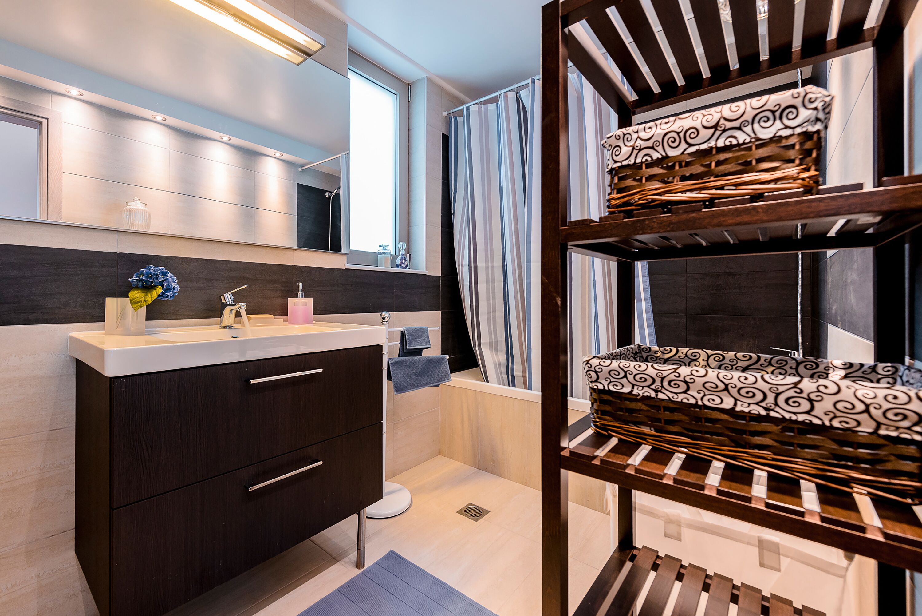 Een moderne badkamer met een donker houten wastafelmeubel, een spiegel en een douchegordijn met strepen.