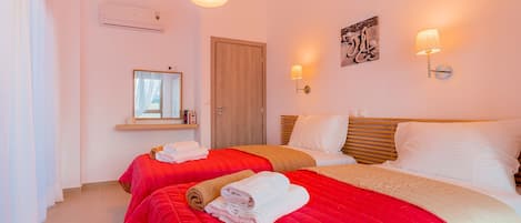 A hotel room with two beds, each with red and beige bedding, a wooden door, a mirror, and wall-mounted lights.