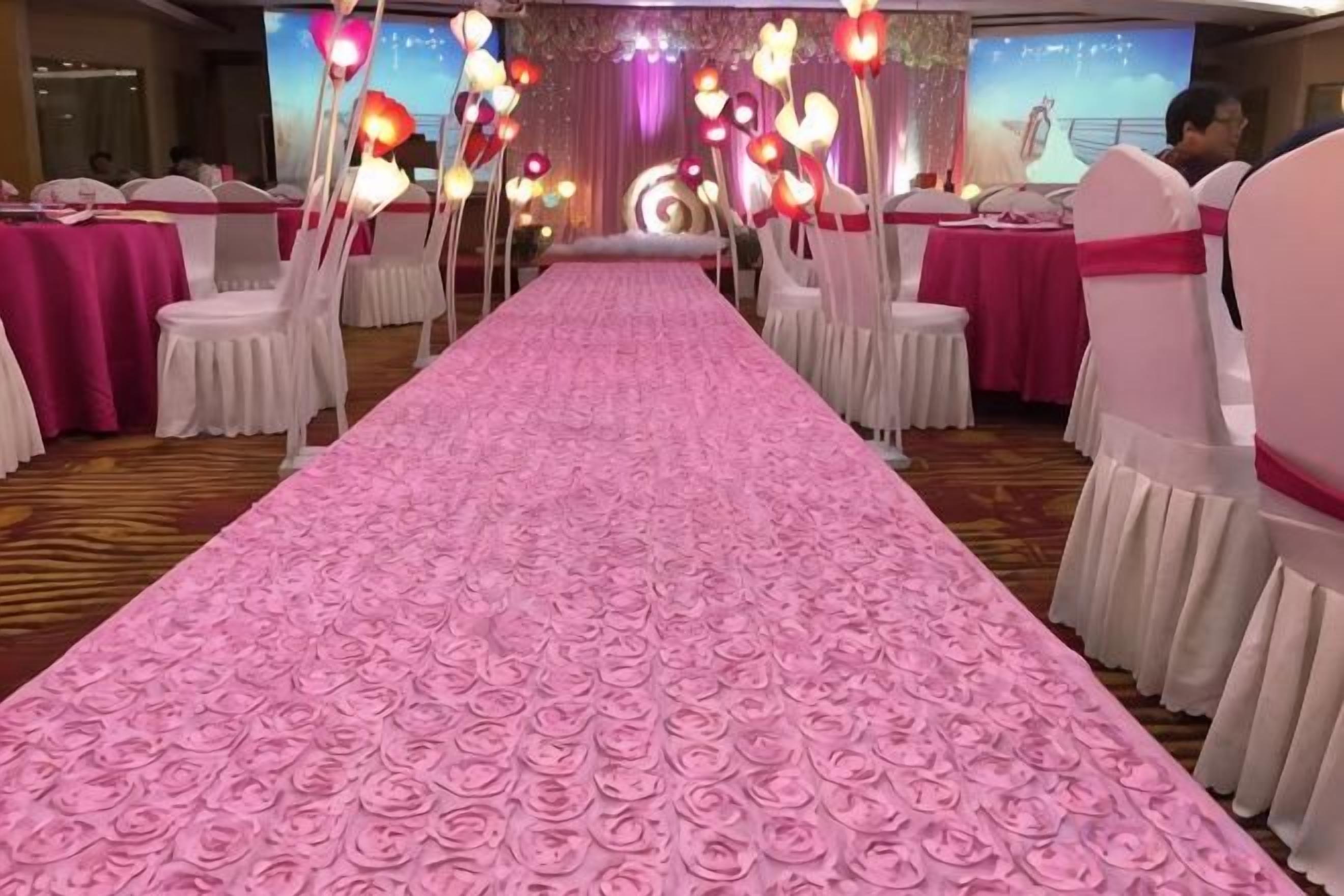 A banquet hall with a pink floral carpet, white chairs, and tables set for a formal event.