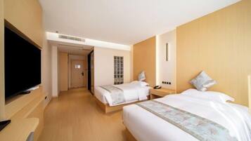 Quarto de hotel com duas camas, televisão e piso de madeira.