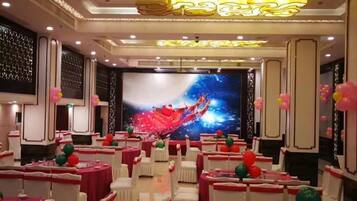 A banquet hall with round tables, white chairs, and a large screen displaying a colorful abstract image.