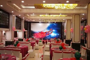 A banquet hall with round tables, white chairs, and a large screen displaying a colorful abstract image.