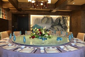 A round table set for a meal with a floral centerpiece, surrounded by chairs with blue glassware. - Fulaidun Business Hotel (Ningbo Airport Yadu Subway Station) (NINGBO)