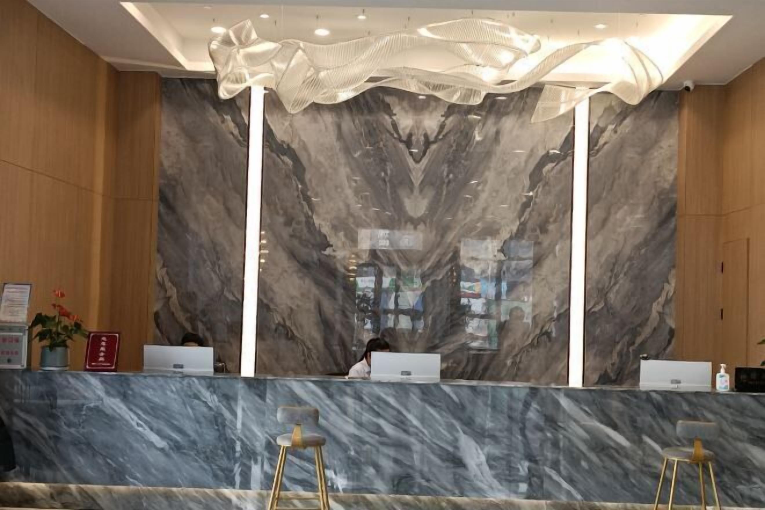 A reception area with marble walls, a modern chandelier, and a counter with two laptops.