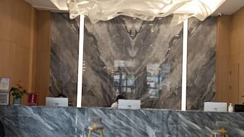 A reception area with marble walls, a modern chandelier, and a counter with two laptops.