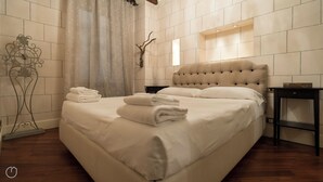 A neatly made bed with folded towels, a decorative wall clock, and a bedside table with a lamp. - Italianway   - Argelati (Milan)