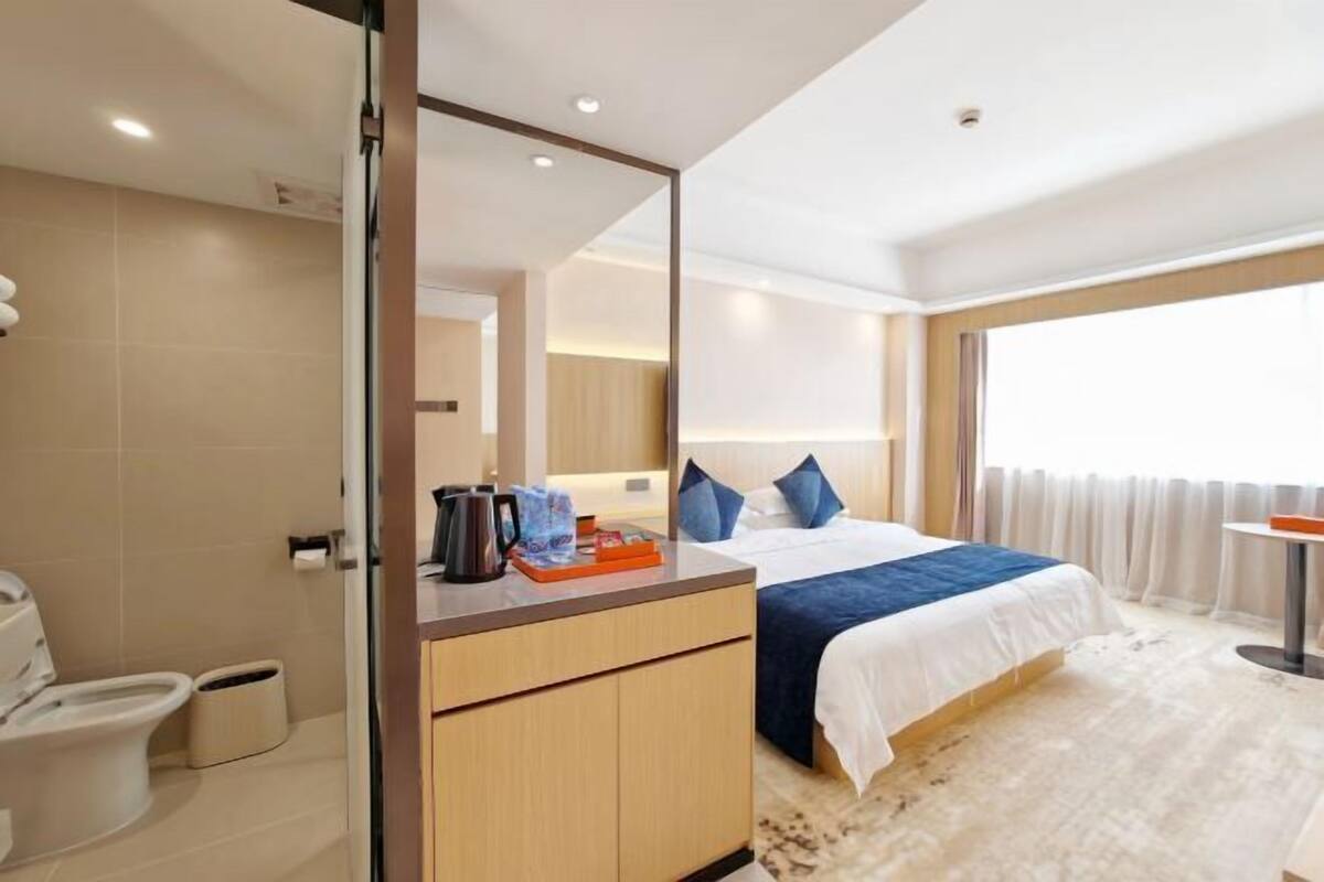 Habitación de hotel con cama, escritorio, espejo, inodoro y ventana.