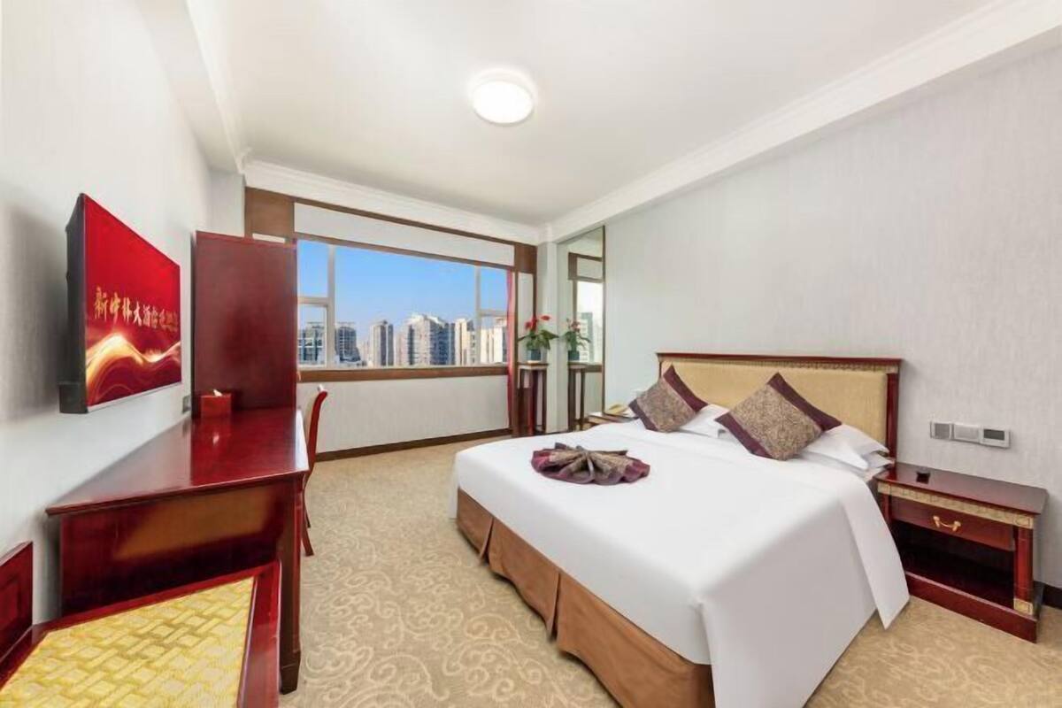 Habitación de hotel con una cama grande, un escritorio, una silla y un televisor en la pared.