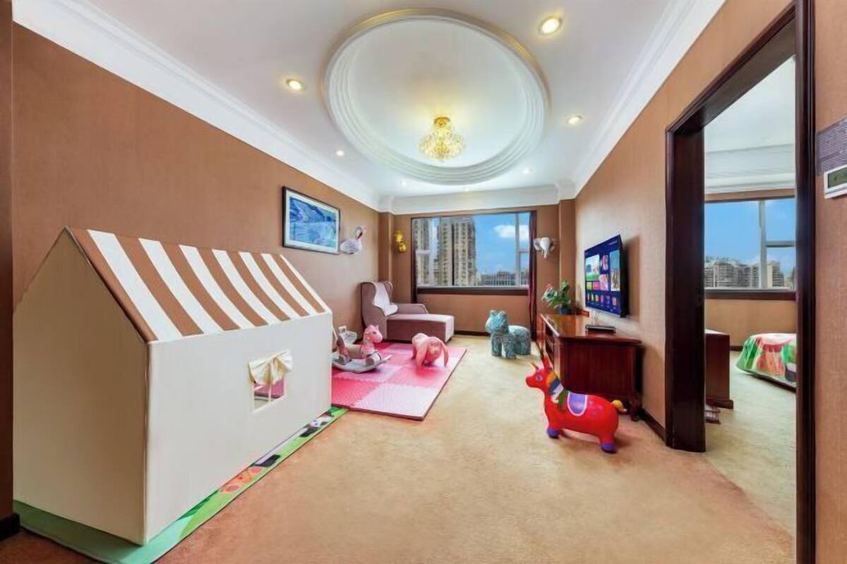 Zona de juegos infantiles con una casita, juguetes y un amplio ventanal con vistas a la ciudad.