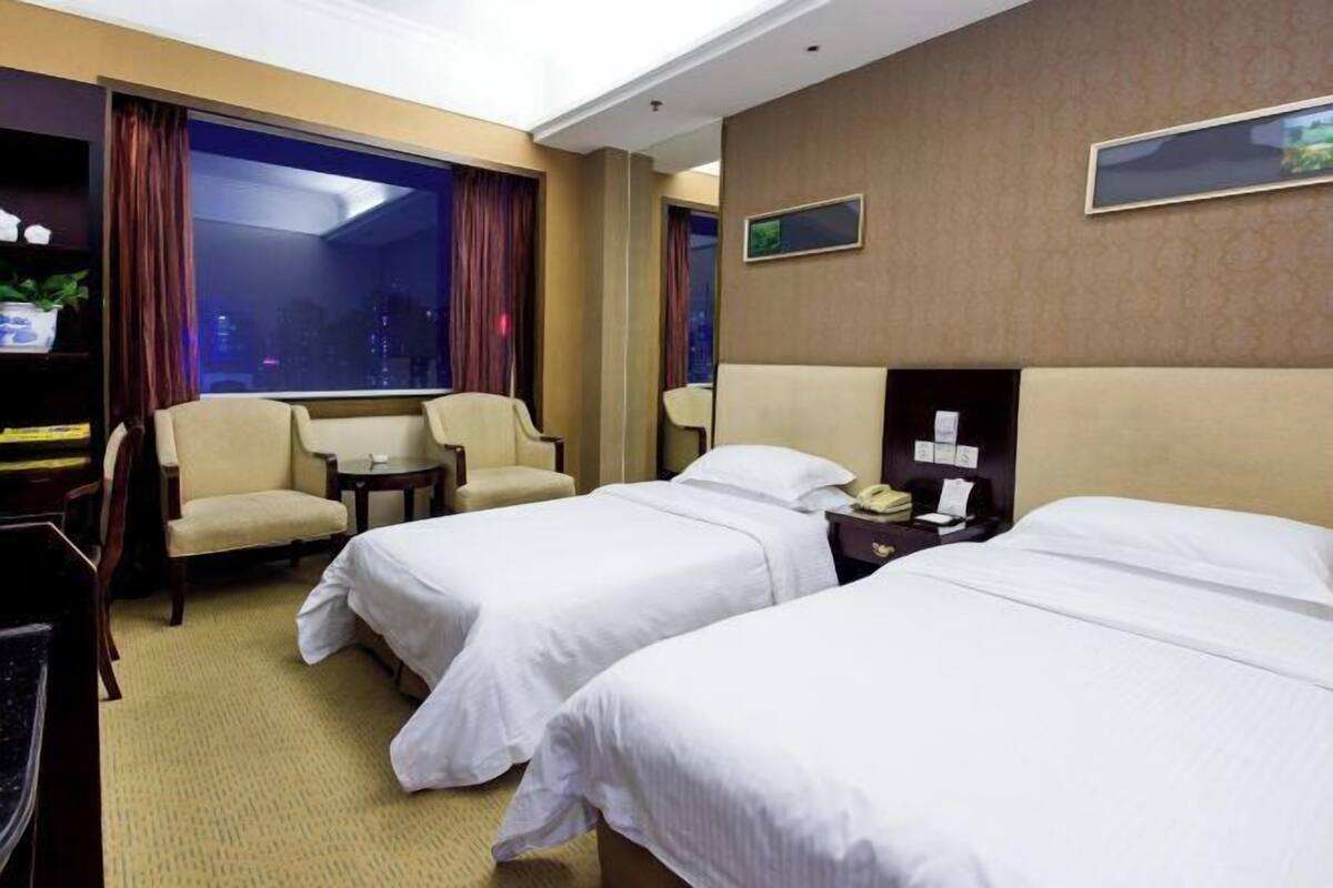Habitación de hotel con dos camas, un escritorio, una silla, una mesita y una ventana con cortinas.