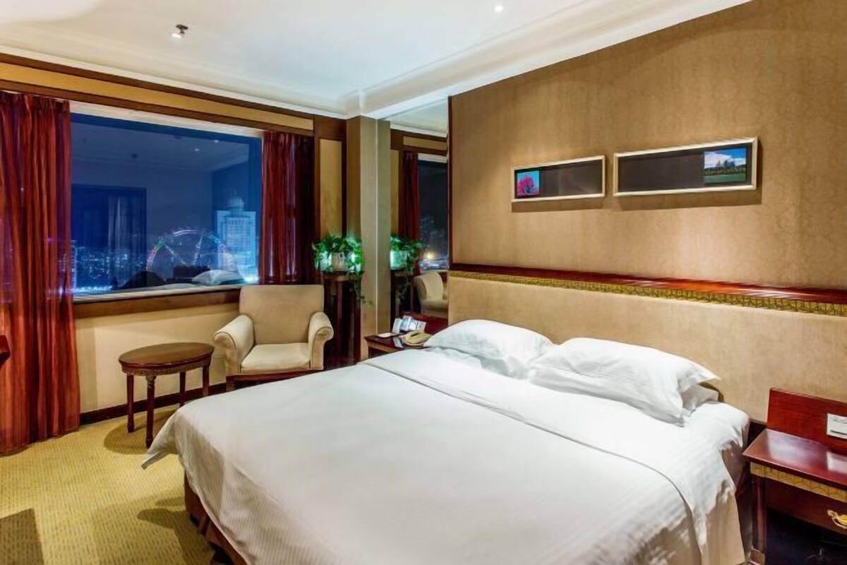 Habitación de hotel con una cama grande, dos sillones, una mesita y vistas a un paisaje urbano por la ventana.