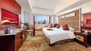 Ein Hotelzimmer mit Bett, Schreibtisch, Stuhl, Fernseher und Fenster mit Blick auf die Stadt.