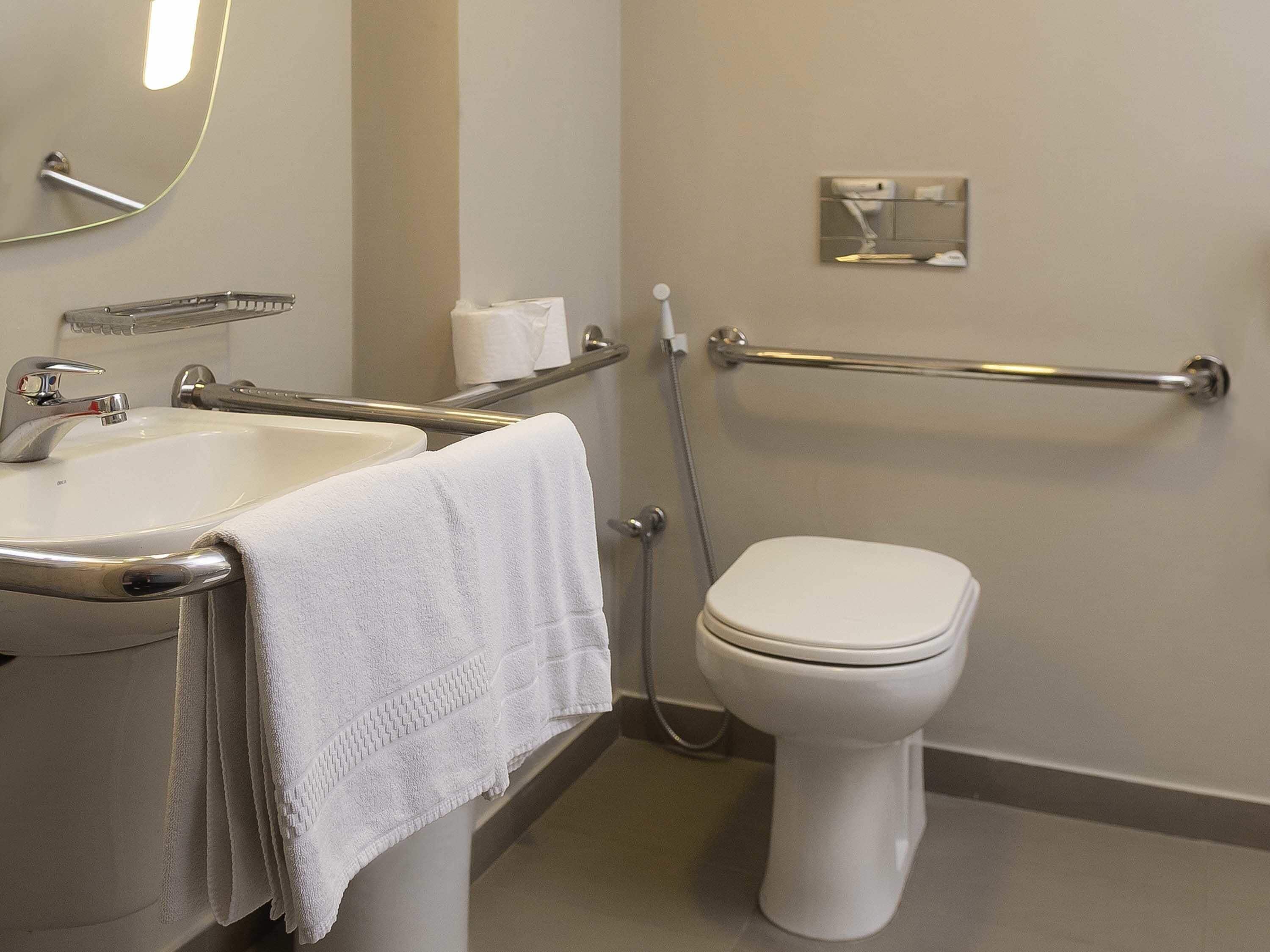 A bathroom with a white sink, a toilet, a handrail, and a towel.