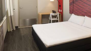 Habitación de hotel con cama, escritorio con teléfono, silla, lámpara y pared decorada en rojo.