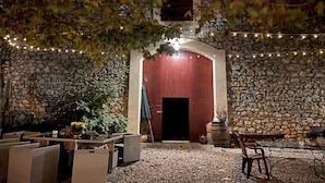Un patio al aire libre con paredes de piedra, luces colgantes y mobiliario exterior.