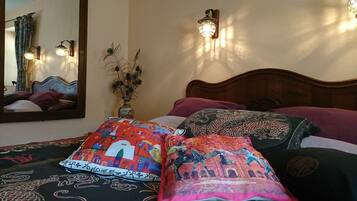 Experience a traditional bedroom with a bed, mirror, and classic headboard, complemented by decorative pillows and a vase with dried plants.