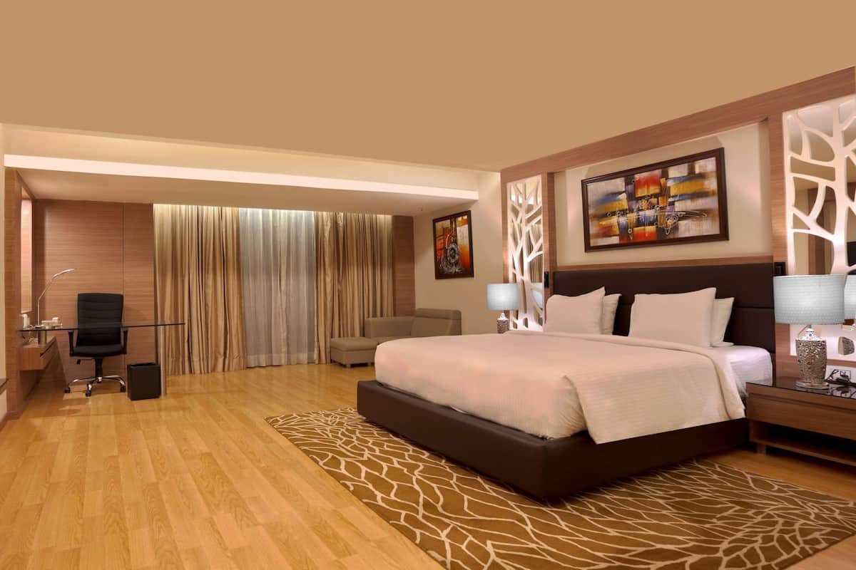 A hotel room with a large bed, a desk with a chair, a television, and a view of the outside through the curtains.