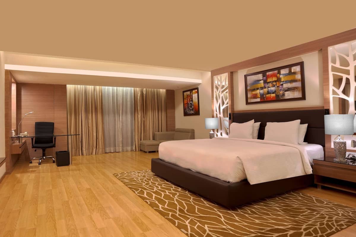 A hotel room with a large bed, a desk with a chair, a television, and a large window with curtains.