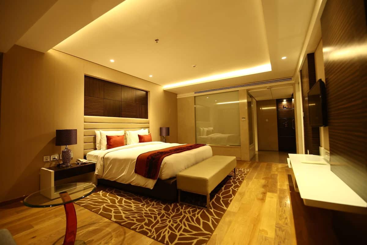 A modern hotel room with a large bed, a glass shower enclosure, and a flat-screen TV.