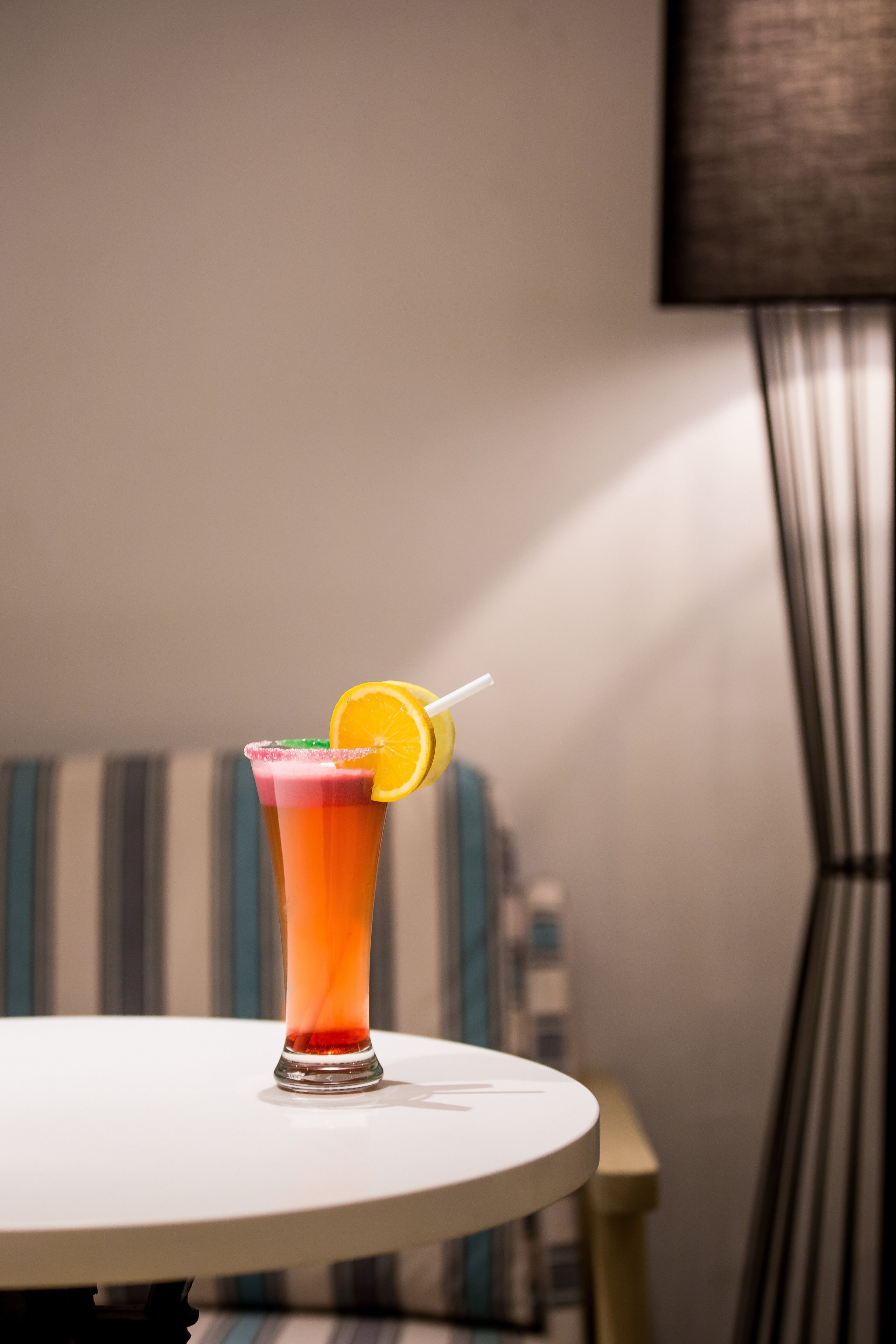 A cocktail on a white table with a striped couch in the background.