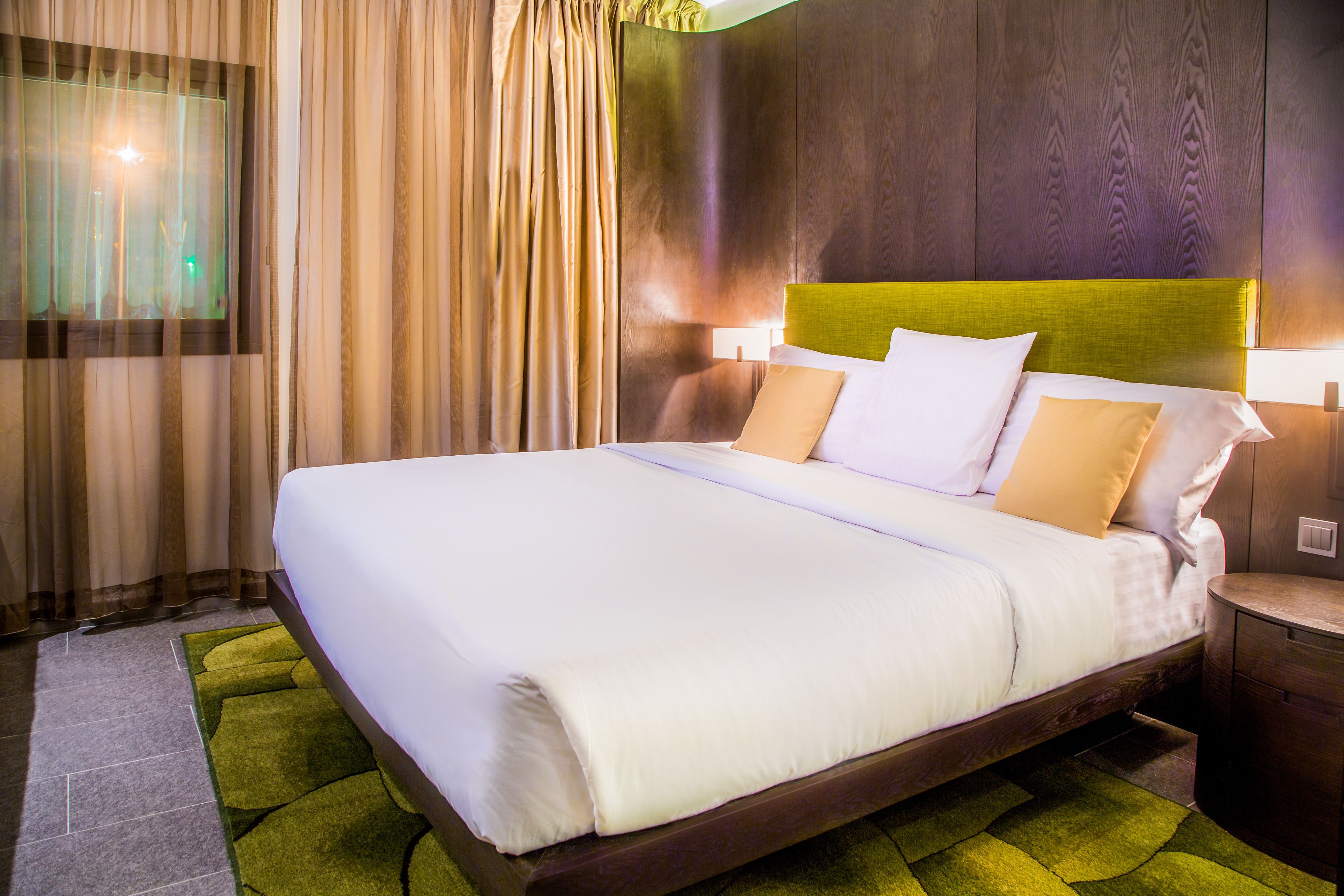 Habitación de hotel con una cama grande, cabecero de madera y alfombra verde.