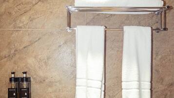 A bathroom with a marble floor, a towel rack with two towels, and two bottles of shower gel and shampoo.