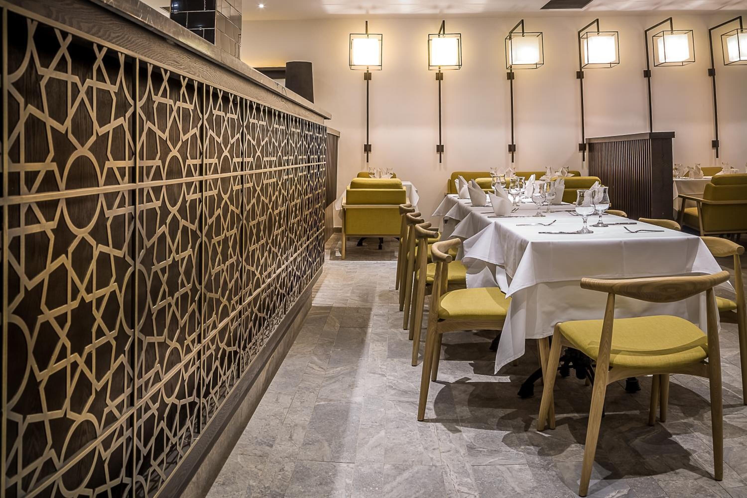 A dining area with round tables, yellow chairs, and white tablecloths.