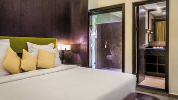 A hotel room with a large bed, a wooden headboard, and a glass shower door.