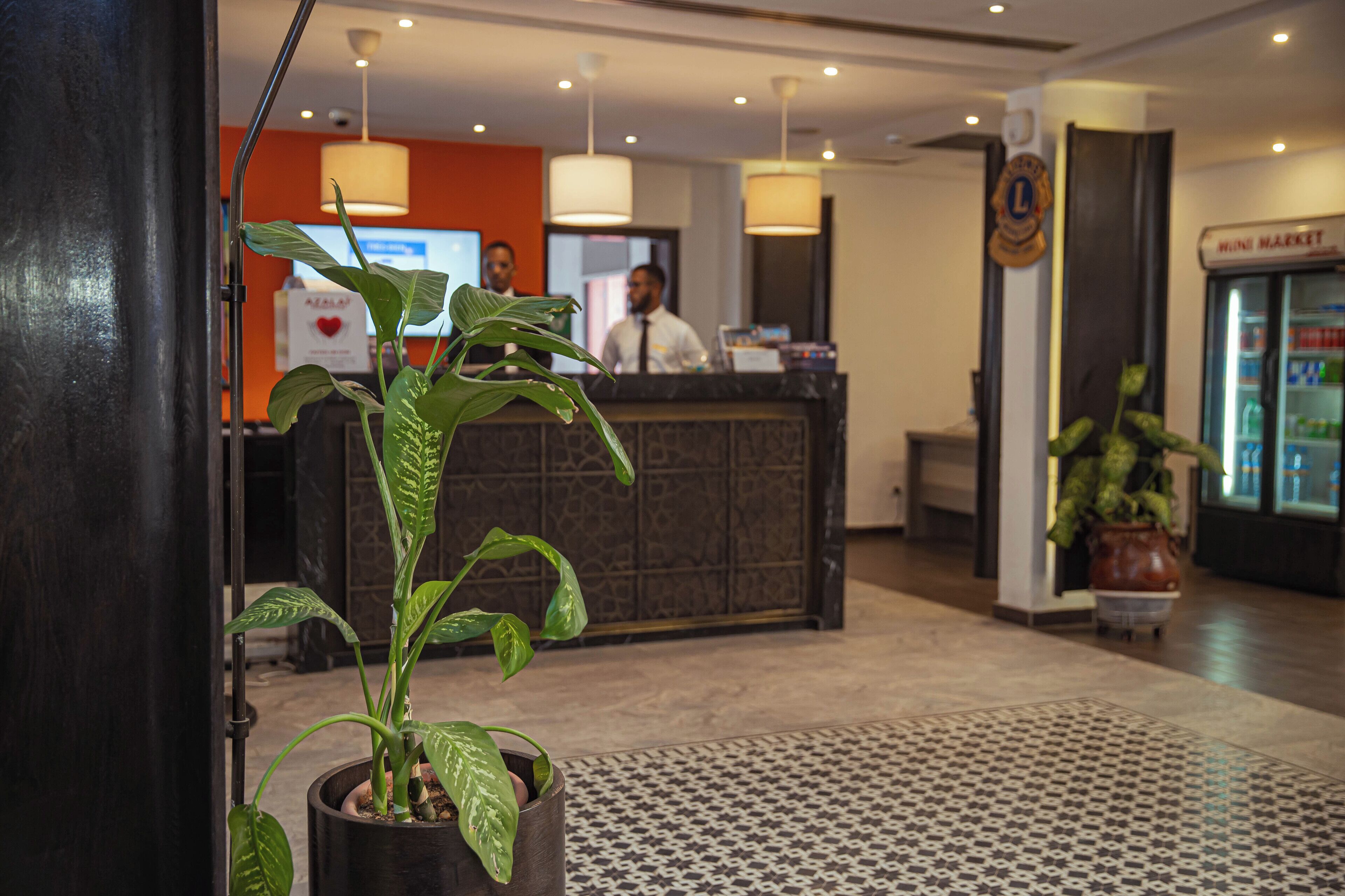 Un área de recepción con mostrador, una planta en maceta, suelo estampado y un cartel de tienda de conveniencia.