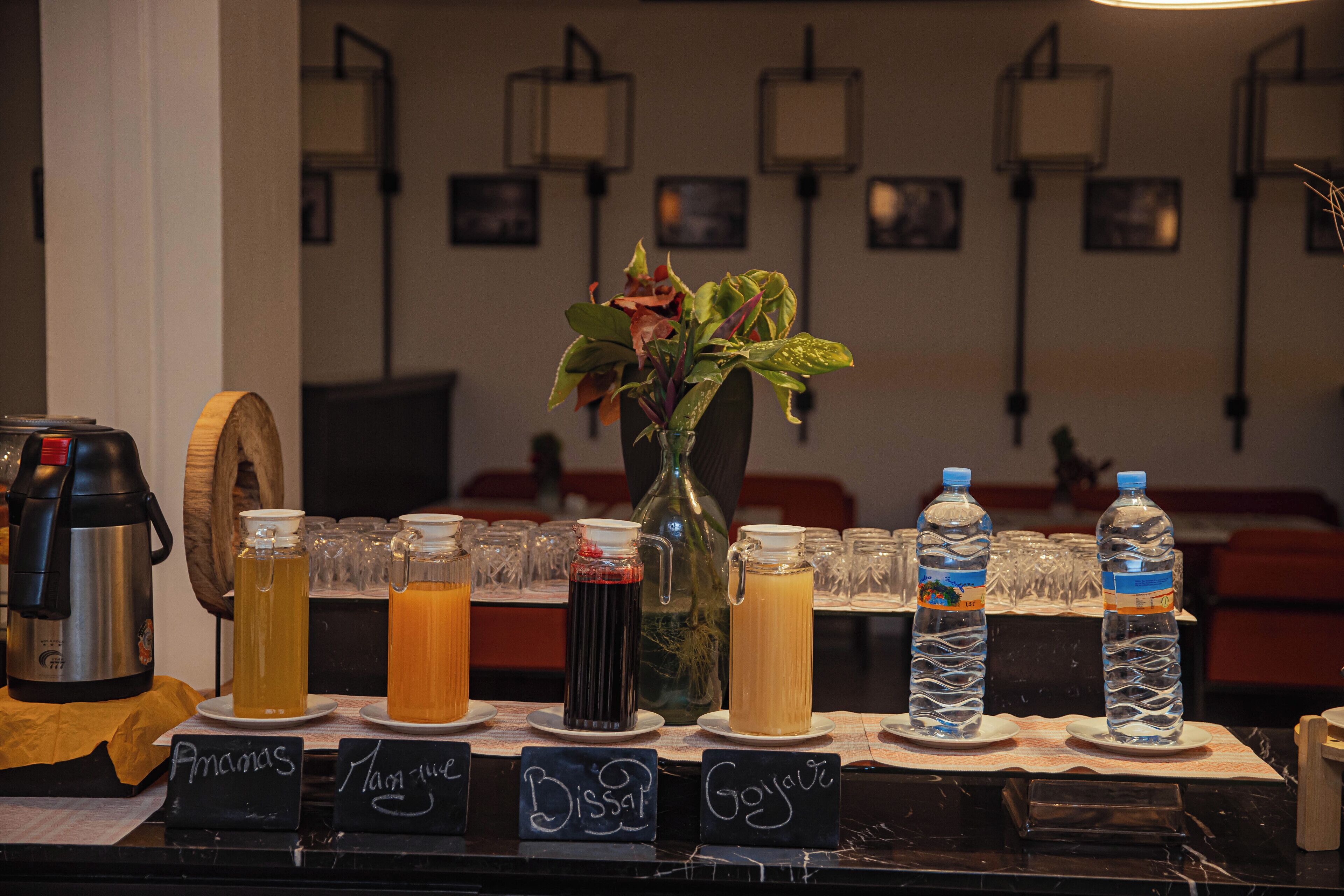 Una estación de bebidas con diversas opciones, botellas de agua, una cafetera y un florero con flores.