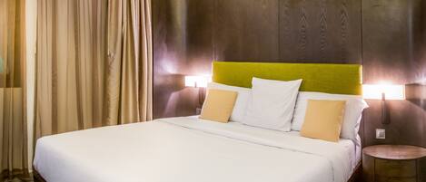 A hotel room with a large bed, green carpet, wooden headboard, and two bedside tables.