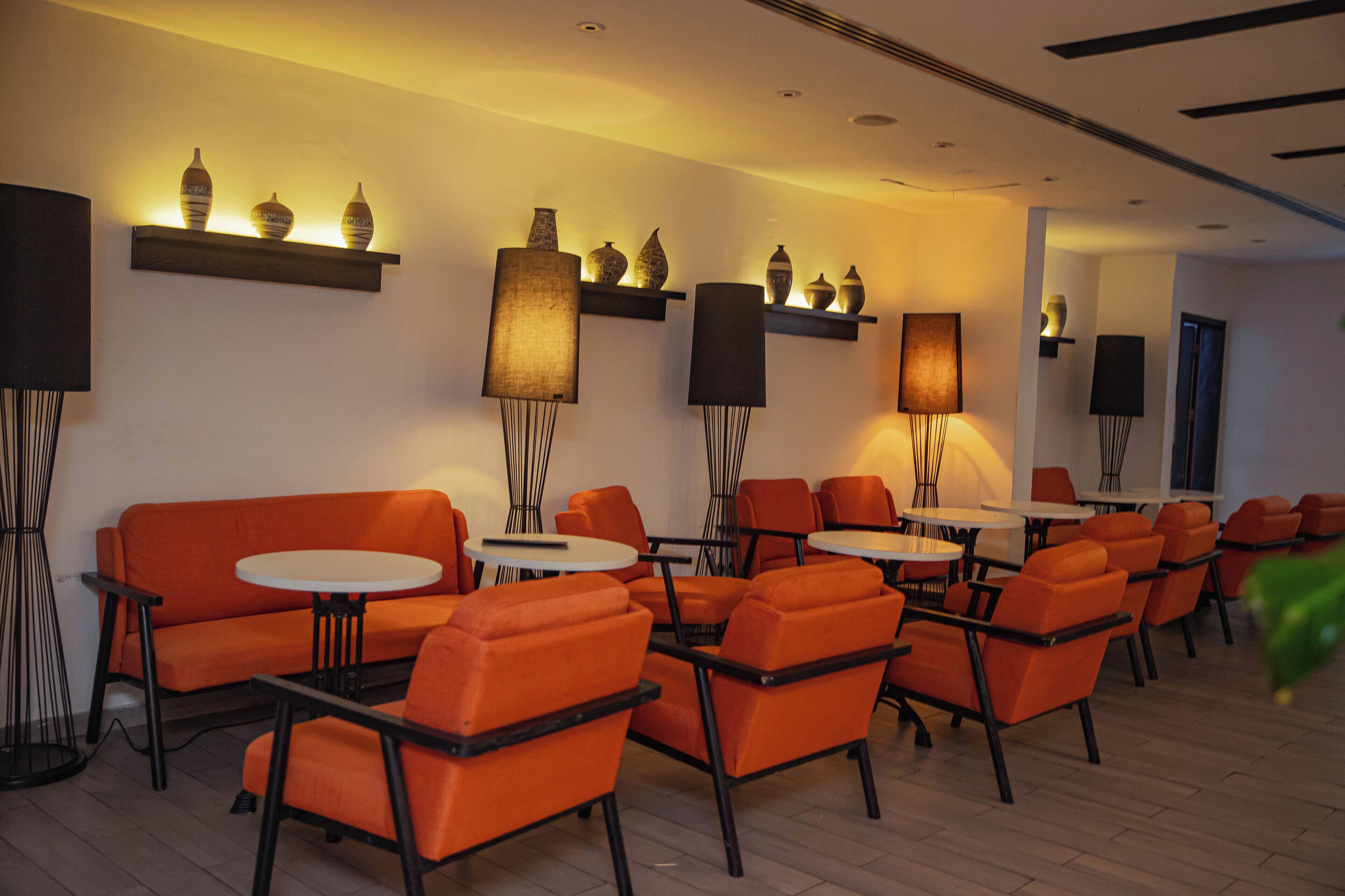 A modern lounge area with orange seating, round tables, and wall-mounted lamps.