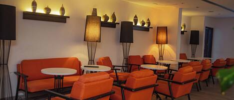 A modern lounge area with orange seating, round tables, and wall-mounted lamps.