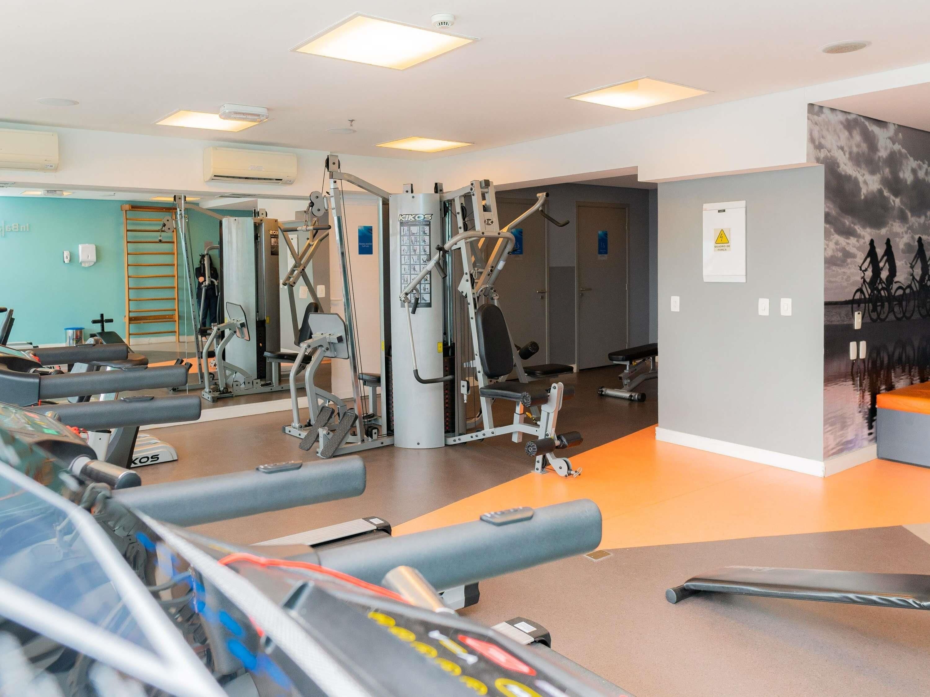 Un gimnasio con máquinas de cardio, equipo de entrenamiento con pesas y una pared con un mural de ciclismo.