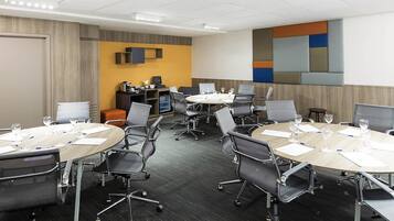 Una sala de conferències amb taules rodones, cadires i una pantalla de projector.