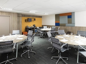 A conference room with round tables, chairs, and a projector screen. - Novotel Santos Gonzaga (Santos)