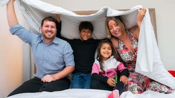 A family of four on a bed with a white sheet and a blanket.