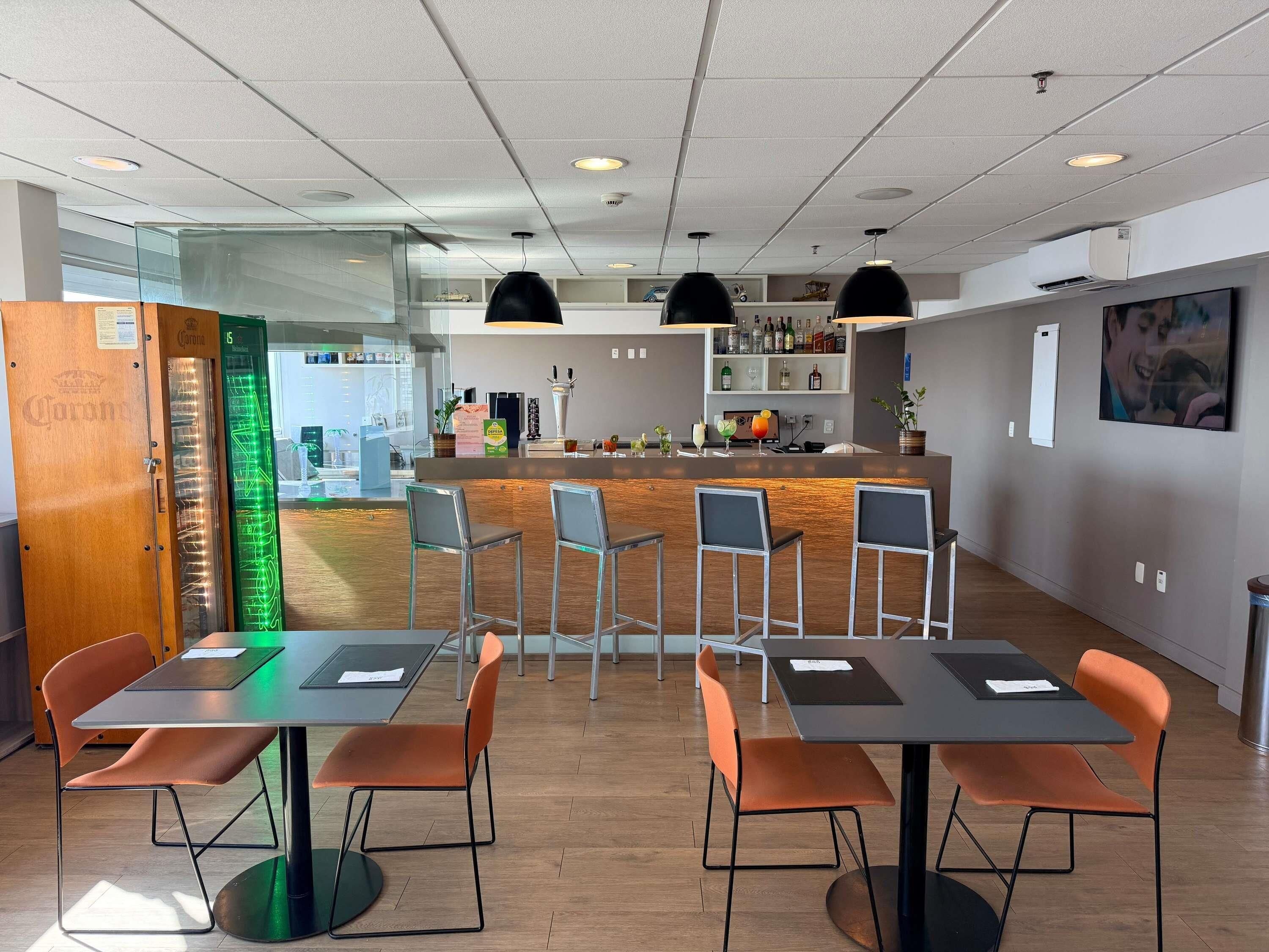 Un espace bar moderne comprenant un comptoir, des tabourets de bar et un coin salon avec des tables et des chaises.