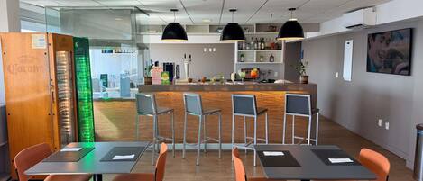 Un área de bar moderna con mostrador, taburetes y una zona de estar con mesas y sillas.