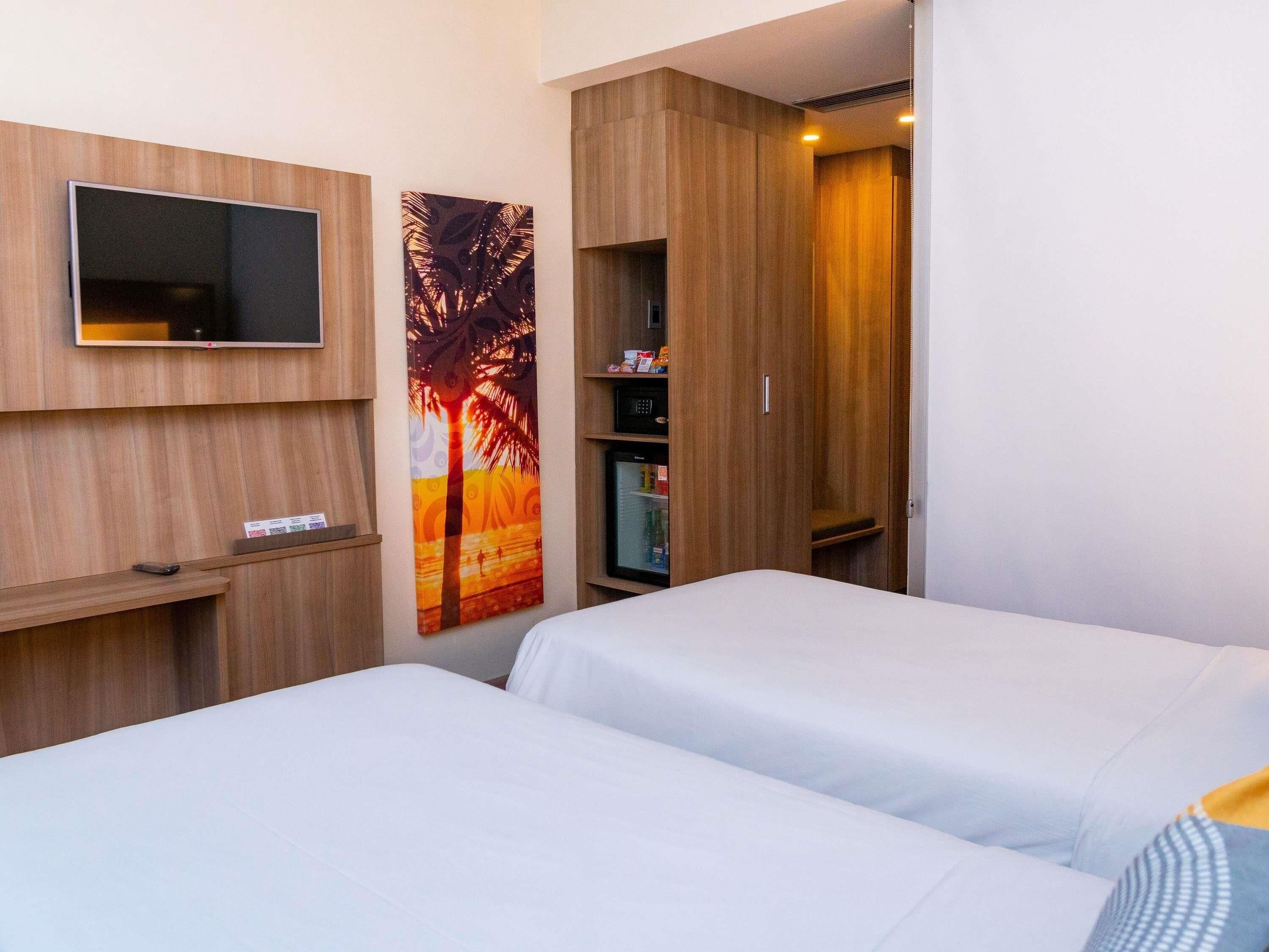 A hotel room with two beds, a TV, a painting, and a wardrobe.