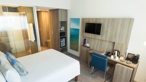 A hotel room with a bed, a desk, a TV, a mini-fridge, and a wardrobe. - Novotel Santos Gonzaga (Santos)