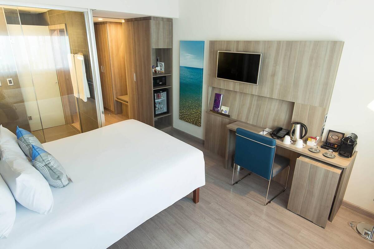A hotel room with a bed, a desk, a TV, a mini-fridge, and a wardrobe.